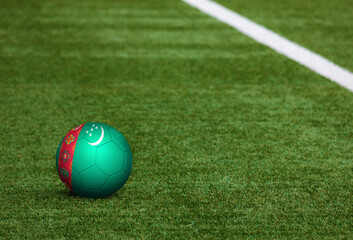 Fototapeta na wymiar Turkmenistan flag on ball at soccer field background. National football theme on green grass. Sports competition concept.