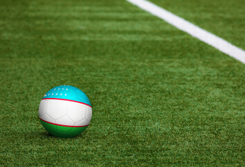 Uzbekistan flag on ball at soccer field background. National football theme on green grass. Sports competition concept.