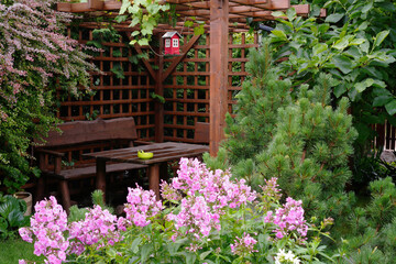 Fototapeta na wymiar wet wooden gazebo with furniture in the garden with flowers