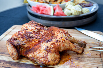 Seasoned and barbecued chicken on cutting board with sides of vegetables and pasta dishes