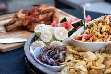 Seasoned and barbecued chicken on cutting board with sides of vegetables and pasta dishes