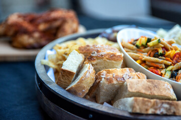 Seasoned and barbecued chicken on cutting board with sides of vegetables and pasta dishes