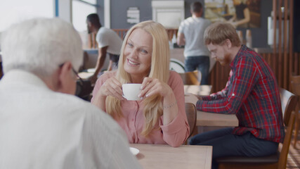 Mature couple sitting at table and drinking coffee in modern cafe