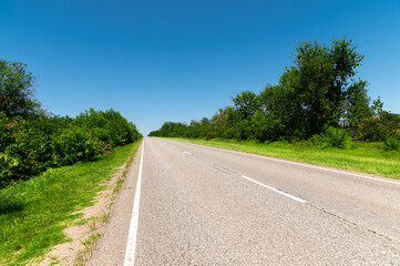 Fototapeta premium suburban empty road asphalt surrounded by trees and grass. The concept of transportation and travel. Background green grass asphalt and blue sky
