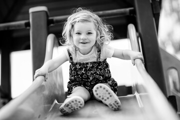 Cute toddler girl playing on slide on outdoor playground. Beautiful baby in colorful shorts...