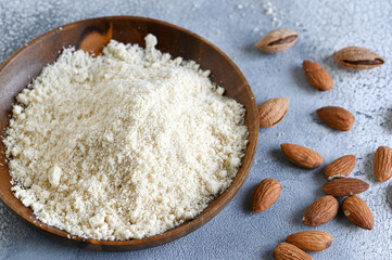Almond flour in a wooden bowl, almonds on old light background