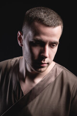Obraz premium Portrait of a strong and large male masseur in special clothes with a finger at the temple reads your chin and knows all your diseases on a black background in the studio.