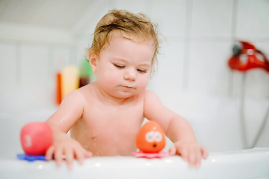 Cute adorable baby girl taking foamy bath in bathtub. Toddler playing with bath rubber toys. Beautiful child having fun with colorful gum toys and foam bubbles