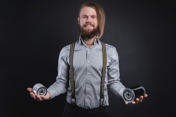 Portrait of a stylish bearded long-haired male salesman and dealer spare parts of the car in a shirt and suspenders. Holding two oil filter selection