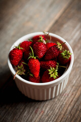 Red ripe strawberry in white bowl on the rustic background. Selective focus. Shallow depth of field.