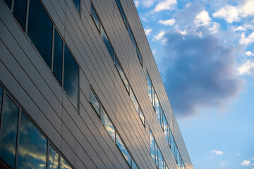 Fototapeta na wymiar Fachada de un edificio de oficinas cuyas ventanas reflejan el cielo con nuves al atardecer