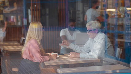 View through window ofn senior couple in love sitting in cafe talking and drinking coffee