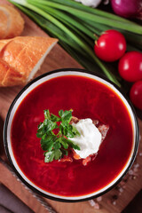 Borscht soup  a on the dark rustic wooden table, with white slices  bread and  sour cream , green onion, view from above