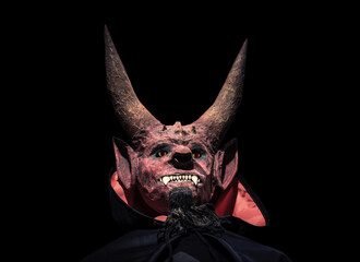Devil with horns and in a black cloak on a dark background looks up.