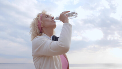Senior woman drinking water after exercising on summer beach