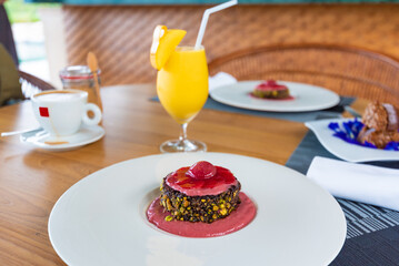 mango smoothie with a piece of mango and a cake with raspberry jam are on the table, an open air restaurant, a glass of juice, a cup of coffee and a jar of coconut sugar