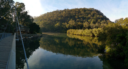 Early morning landscape view of a calm creek with beautiful reflections of blue sky, mountains and trees on water, Cockle Creek, Bobbin Head, Ku-ring-gai Chase National Park, New South Wales Australia