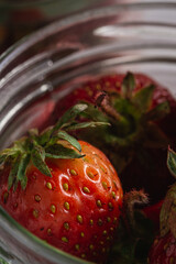 Fresh ripe strawberry fruits in glass jar, summer vitamin berries on grey stone background, angle view macro