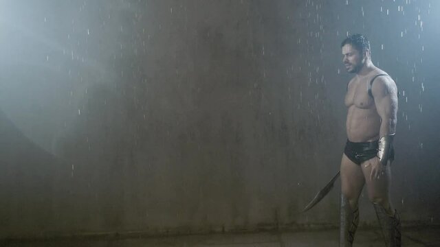 Wet shirtless gladiator jumping in attack.