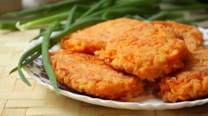 vegetarian dish of carrot cutlets with fresh green onions in a white plate with blue ornaments located on a wicker bamboo tablecloth