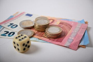 There are a few banknotes and euro coins to be seen. Next to is a cube with a six.
