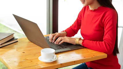 A young business woman wearing a red shirt is working on a laptop and having a coffee cup next to him.