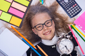 Portrait of a little schoolgirl in glasses in a frame from school supplies.