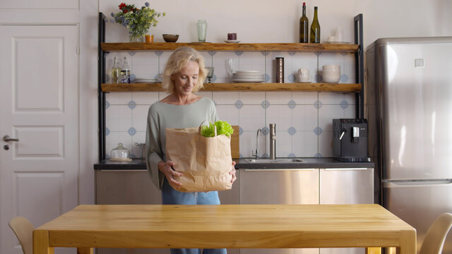 Mature Woman Returning Home From Shopping Trip Unpacking Groceries