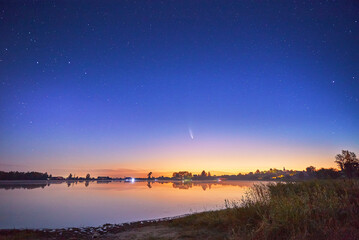 Neowise comet with light tail in night sky over lake