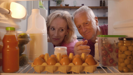 Aged married couple taking container with fresh cherries from refrigerator
