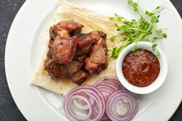 Fried shish kebab with lavash, sauce, microgreen and onion, on a white plate, on a gray background