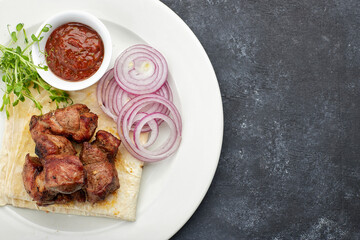 Fried shish kebab with lavash, sauce, microgreen and onion, on a white plate, on a gray background