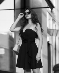 Elegant woman wearing black dress. Outdoor portrait. Pretty beautiful stylish girl with wavy hair. Caucasian female model.