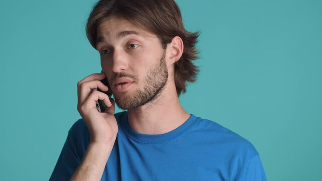 Young casual calm man indignantly talking on phone over colorful background