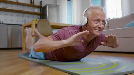 Aged man in headphones training on sport mat at home