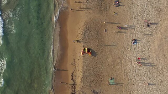 Sunset at the beach with people walking and Kite surfers enjoying last moments of Sun, Aerial view.
