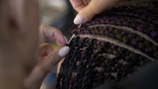 Hairdresser's female hands professionally braiding a pigtail with a hook close up. Braiding. Professional doing afro pigtails. Head of a woman with afro braided hairs 