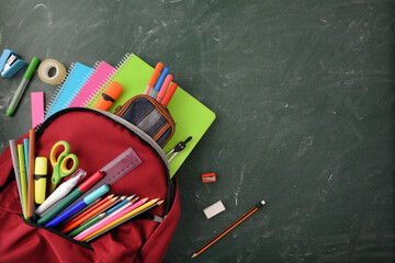 Fototapeta na wymiar Backpack full of school supplies on green blackboard top view