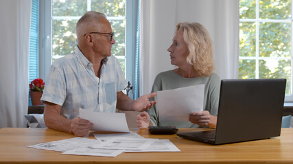 Mature couple sitting and managing expenses at home.