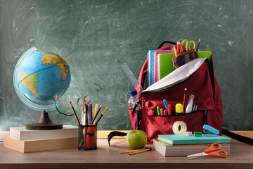 School desk with school supplies and blackboard background front view