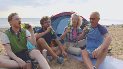 Fototapeta premium Group of friends cheering with beers at barbecue dinner on the beach