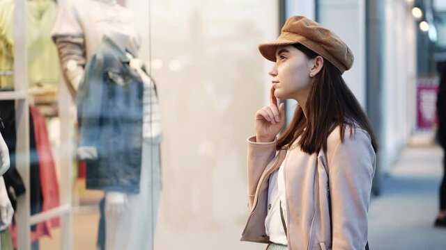 Beautiful young woman looking at the window of luxury store in city shopping center.