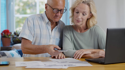 Senior couple at home discuss income and pay bills online scanning qr-code