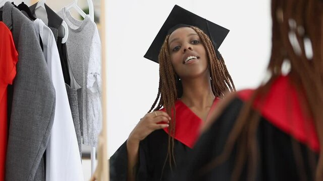 woman put on graduating cap and gown and look in mirror Spbi. african american female finish education. proud achievement. enthusiastic 20s black girl. college university ceremony