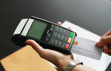 A woman using hand credit card swipe machine for sell products in the shop. Concept of spending via...