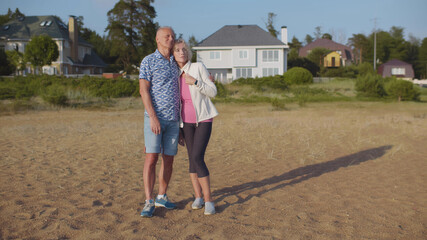 Senior couple embracing on beach near country house enjoying vacation