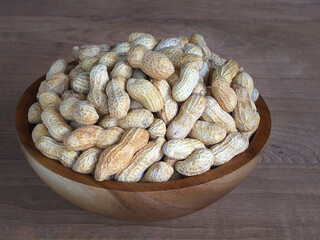 Dried peanuts in a wooden bowl, placed on a wooden floor