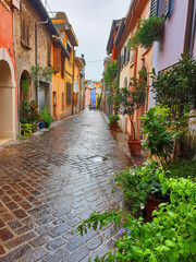 Fototapeta na wymiar A colorful, narrow, deserted street in Rimini on a rainy, overcast day. Vertical photo of a colorful, wet street in a tourist city in Italy.