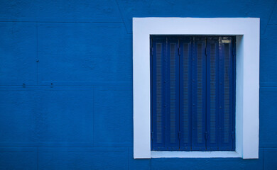 Window with blue metal closed shutters on a blue wall, close view