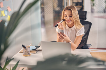 Cheerful young woman doing makeup at work